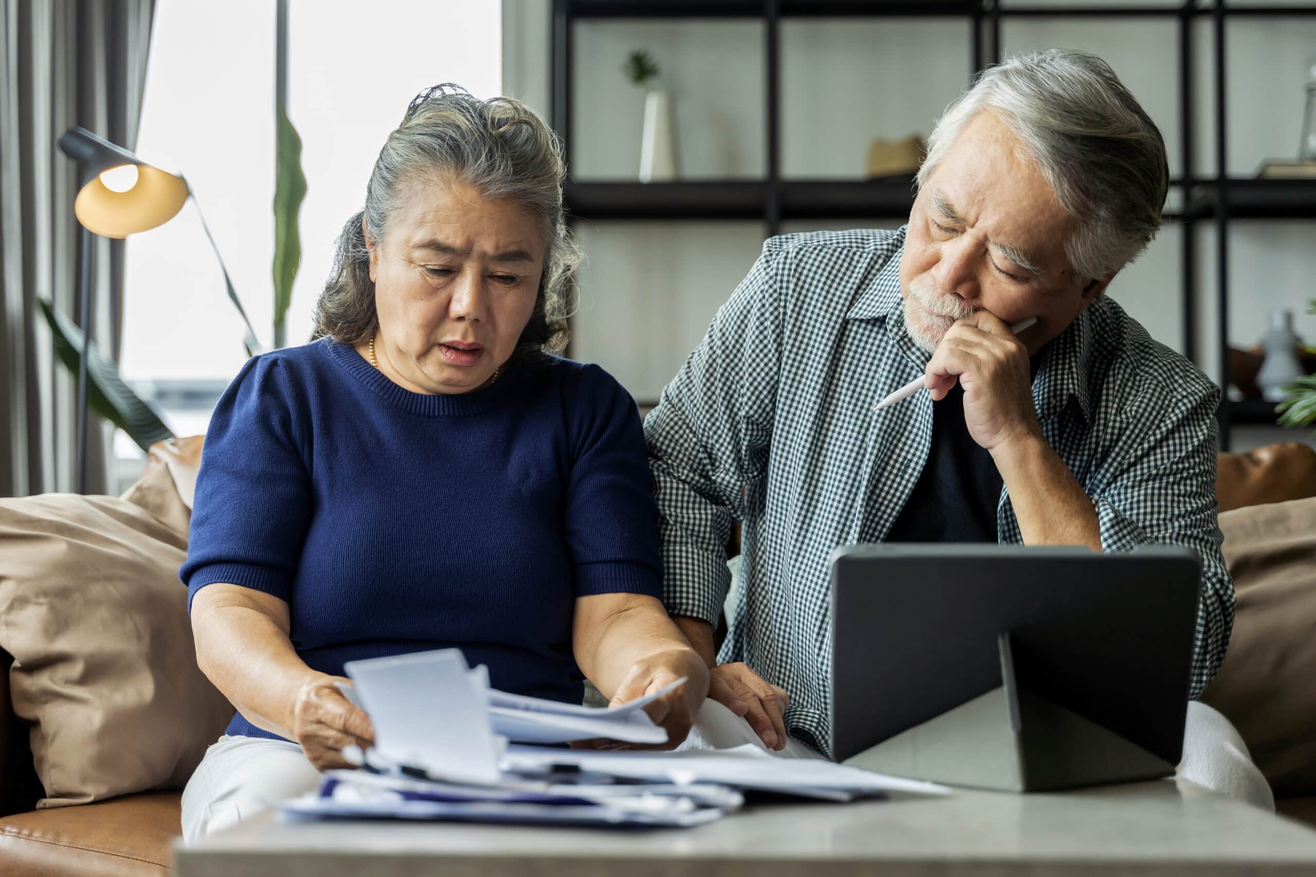 Asian couple looking frustrated at computer and bills