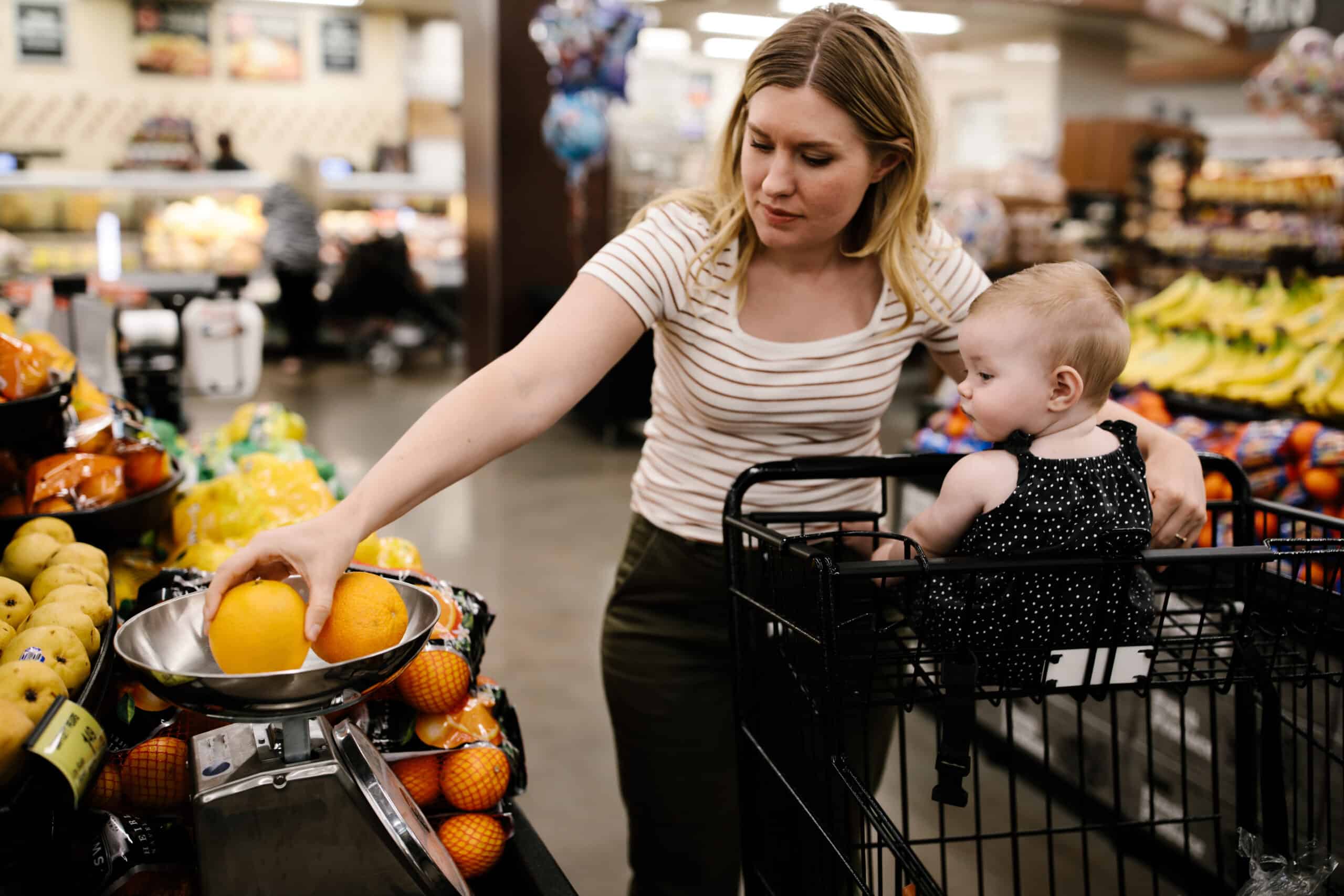 Woman grocery shopping with a cart with her baby in it