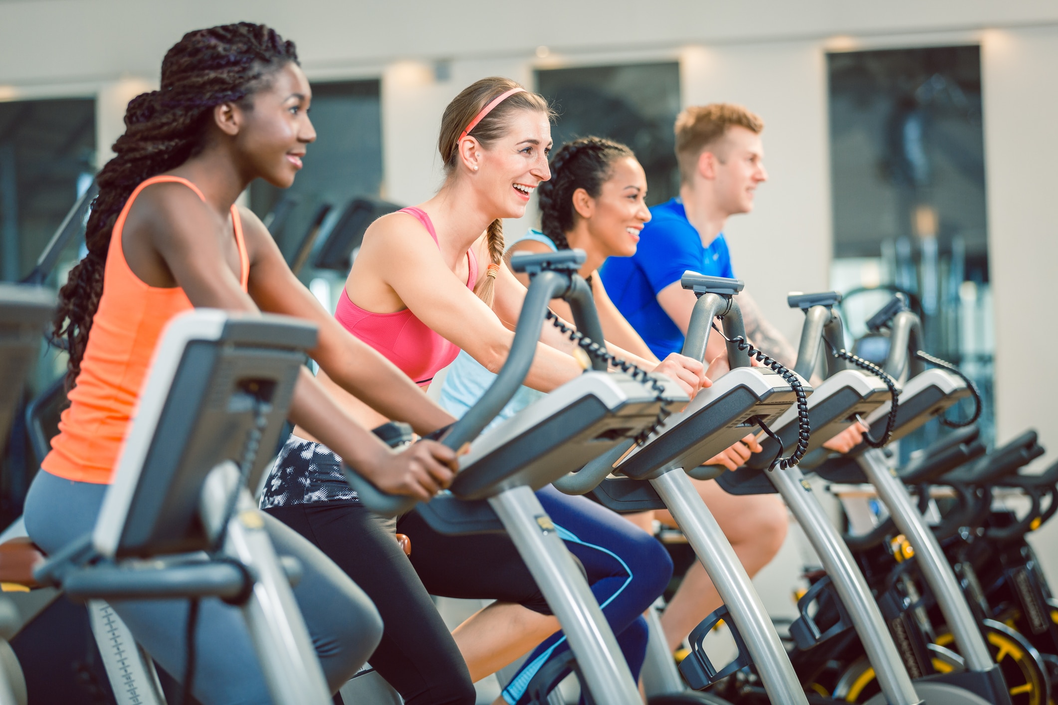 Average gym membership cost. brunette beautiful woman smiling while cycling on a modern fitness bicycle during group exercising class at the gym